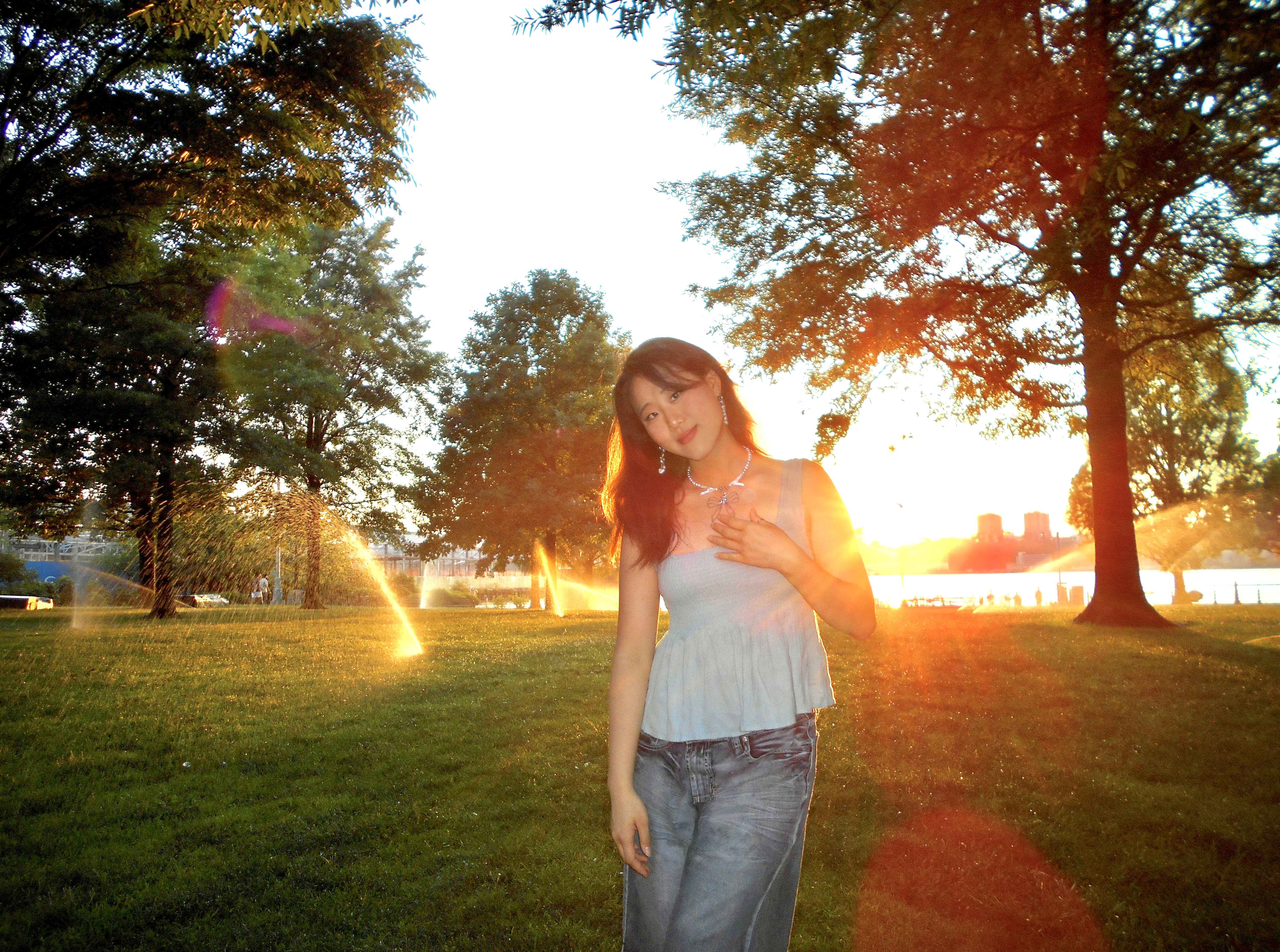 Rebekah Zhao Person standing in a park at sunset, with sunlight flaring through the trees.